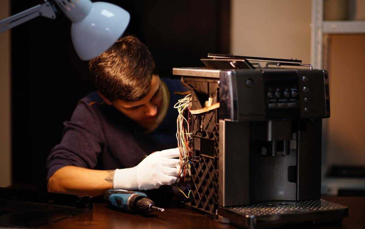 Homem fazendo manutenção em uma máquina de café expresso desmontada